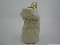 Side view of cream-colored Belleek girl-shaped creamer pitcher with detailed bonnet and dress folds.