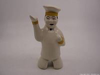 Front view of the white ceramic pie vent figurine of a baker, with yellow and black painted details, showing overall condition.