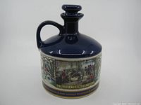 Front view of the porcelain decanter showing overall form and handle, dark blue top, and one of the painted scenes.