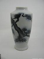 Front view of white glazed porcelain vase with black tree branch and pine needle decoration, showing tapered shape and neck.