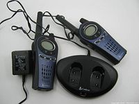 Two Cobra MicroTalk walkie talkies placed upright in the charging dock along with the power adapter plugged in showing the entire lot.