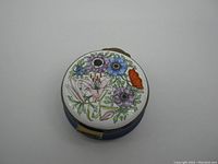 Top view of the enamel trinket box lid featuring colorful flowers painted in enamel on white background.