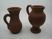 Front and side view of two red clay pottery jugs, showing shape and details including flake on larger jug spout.