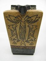 Front view of rectangular ceramic pitcher with brown textured surface and black Aztec-style bird and fish designs, signed Laurel Burch near the base.