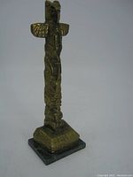 Front view of solid brass native indigenous totem pole showing carved figures and bird top on a stone base.