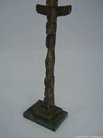 Front view of solid brass native indigenous totem pole mounted on square stone base, showing carved bird figure at top and multiple carved faces and symbols along the pole.
