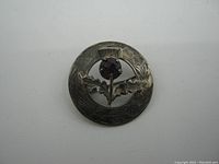Front view of the sterling silver Scottish brooch showing purple stone thistle in center and engraved detailed circular frame.