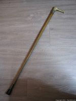 Full length of the wood cane showing the entire shaft and rubber tip against a wooden floor background.