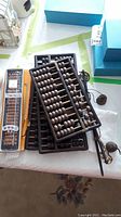 Five abacus including three large wooden abacus with black beads and two smaller boxed wooden abacus with brown beads arranged on table.
