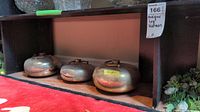 Three brass leg warmers placed beneath a shelf, showing relative sizes and reflections on a red carpet.