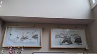 Two rectangular shadow box frames hung side by side on a wall, each containing Asian landscape scenes made with shell inlay.