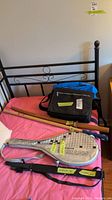 Overview of all items in the lot arranged on a bed with pink sheet; laptop bag, duffle bag, badminton racket with case, Asian decor item, kendo sticks