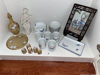 All items displayed on wooden surface including ceramic beverage dispenser, trays, cups, bowls, statue and frame