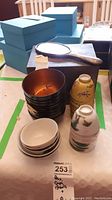 Photo showing wood box, stacks of lacquered wooden bowls, and ceramic cups in varying floral and landscape designs.