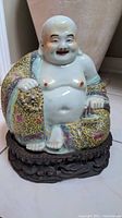 Front view of painted porcelain seated Laughing Buddha on carved wood base