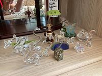 Crystal figurines grouped together on a table including swans, cat, butterfly, decorative glass bottle, castle, and mineral rock.