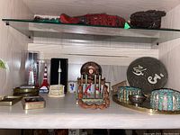 Wide view of travel collectors pieces including trinket boxes, souvenir figurines, decorative plate, and a beaded bracelet.