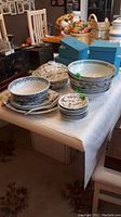 Overview of assorted porcelain plates, bowls and spoons displayed on table with green lot tags.