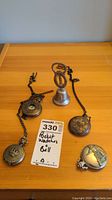 Four pocket watches and one small metal bell arranged on wooden surface, two pocket watches with visible chains and ornate designs, bell with key-like handle and Pisa Italy engraving.