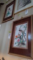 Two framed Asian bird prints hanging on a wall, one with a peacock and one with ducks and flowers.