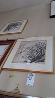 Framed botanical print featuring grass and plants, with gold frame and white mat, showing part of the other print above it on the wall.
