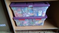 Two clear plastic totes with purple lids filled with assorted children's toys packed inside, showing volume and content transparency.