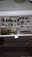 Drawer with multiple sets of silver plated teaspoons and metal stir sticks organized in trays.