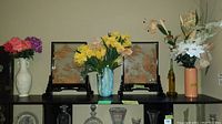 Full view of the three vases with faux flowers and two Asian-inspired wood art panels on a black shelf.