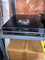 Full view of Sharp VP-3000B VHD video disc player on shelf with remote control on top.