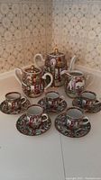 Full view of the Asian porcelain tea service set showing teapot, sugar/tea bowl, pitcher, 5 teacups and 5 saucers arranged on white surface.