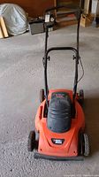 Front view of Black & Decker electric lawn mower with handle and wheels, placed on concrete floor.