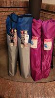 Four camping chairs in fabric carrying bags; two blue-gray bags and two pink bags, each labeled as a folding camp chair.