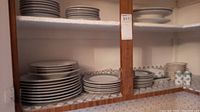 Wide shot of stacked white plates and bowls on shelves showing a variety of dishware sizes and rim patterns
