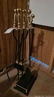 Fireplace tool set with holder, showing gold-tone handles and black metal shaft tools standing in a holder.