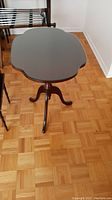 Wood pedestal side table with a uniquely shaped glass top, shown from an angle.