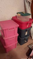 Stack of eight storage totes including three pink, two red, two black, one small clear with green lid