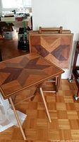 Photo showing one TV tray table set up and three trays stored vertically in a wooden stand, highlighting the geometric wood inlay and foldable leg design.