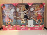 Three Barbie cheerleader dolls in original boxes displayed side by side showing their university-themed cheerleading outfits and packaging.