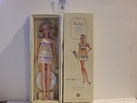 Barbie Silkstone doll in original box with illustrated box cover, doll displayed in cream dress with lavender ribbon details, cream high heel shoes with ankle straps, and white stand inside box.