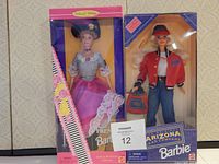 Photo of two boxed Barbie dolls: one Arizona Jean Company Barbie in red jacket and hat, the other a French Barbie in pink and purple historical dress with lace and matching hat.