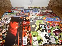 Photo showing over 25 comic books laid out fanned across a surface, featuring various comic book covers including The Punisher and Spider-Man, from multiple publishers.