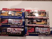 Photo of six boxed diecast mini hauler trucks, four branded Matchbox limited editions featuring Mark McGwire sports themes, and two White Rose branded trucks including a 1978 Packers NFL design and a checkered race car design.