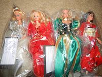 Four Barbie dolls in plastic bags, dressed in festive and cultural outfits, arranged side by side on carpet.
