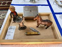 Front view of tray with all items: antique bank, three metal statues (cowboy, horse, painted head), and vintage pocket knife.