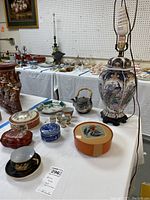 Overview of the lot on white table showing lamp, teacup, teapot, trinket dish, sake cups, plates