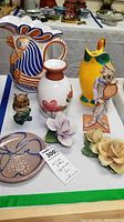 Front view of porcelain florals, tennis player figurine, pitchers, vase with tag showing lot number and description