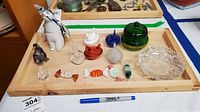 Art glass figurines and collectibles on wooden tray including penguins, hen on nest, glass candies, gilded green jar, and sawtooth crystal bowl.