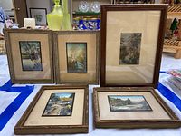 Five framed vintage tinted photos by Wallace Nutting arranged on a blue and white striped cloth, showing size and framing style.