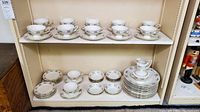 Full view of Haviland china plates stacked and arranged on shelves with teacups, saucers, small bowls, and a sauce boat.