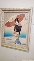 Frontal view of the framed Japanese silk painting picturing a woman with a red parasol.